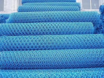 Many blue PVC coated hexagonal wire mesh rolls are piled together.