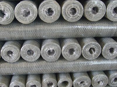 Many galvanized hexagonal wire mesh rolls with film are piled up together.