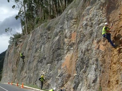 Four people are installing galvanized rockfall netting on cliff.