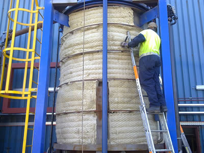 A worker is managing the rock wool blanket over a blue reactor.